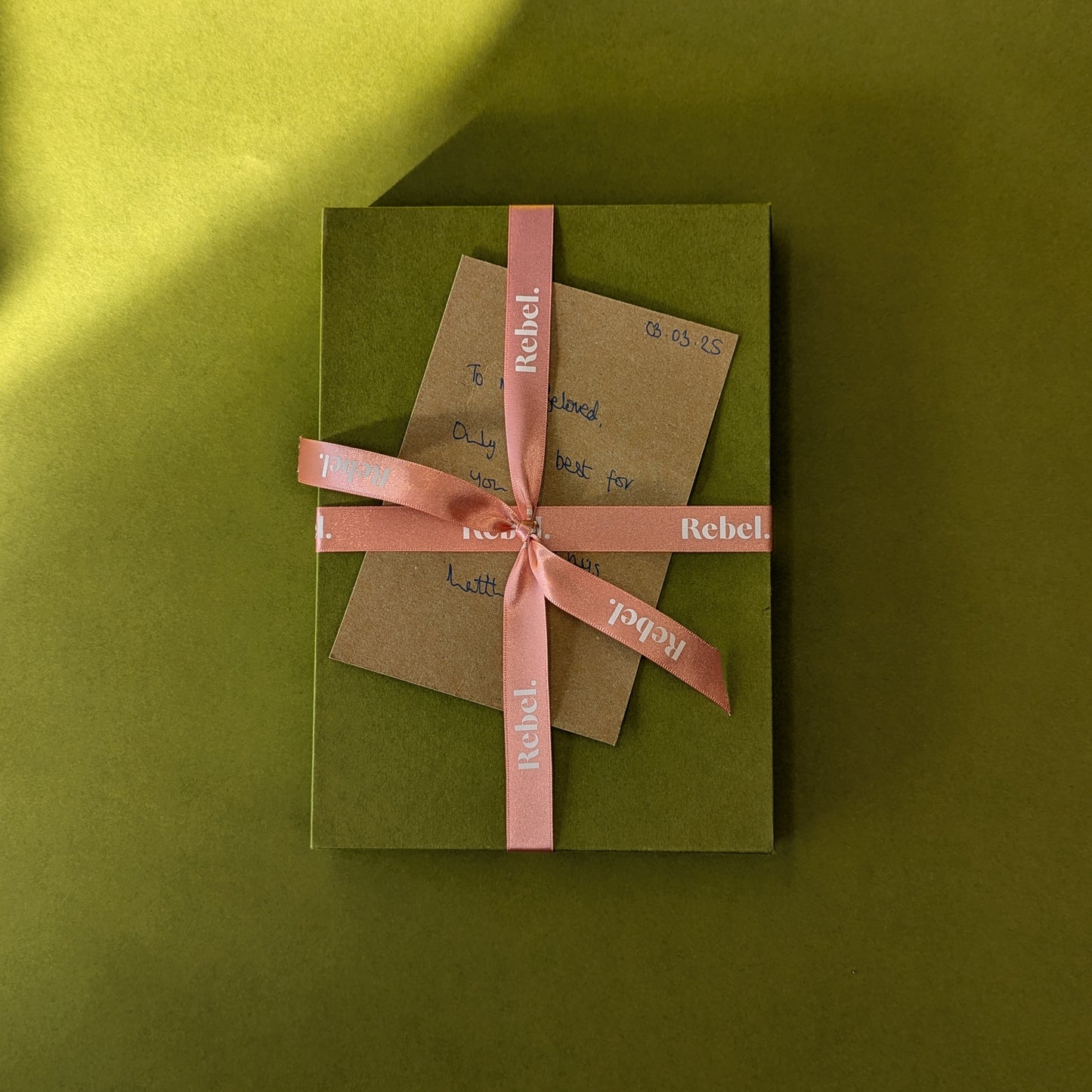 Rebel Stationery's Gift wrap option of green slipcase, branded peach ribbon, and handwritten message on Kraft card, on a green background