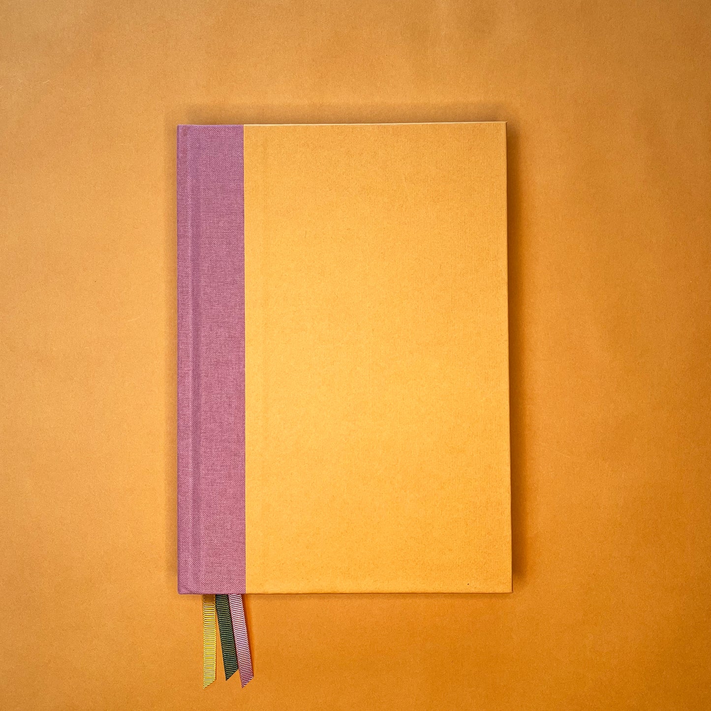 Front cover of Rebel Stationery's Gold Seasonal notebook (yellow cover with pink linen spine) on a yellow background