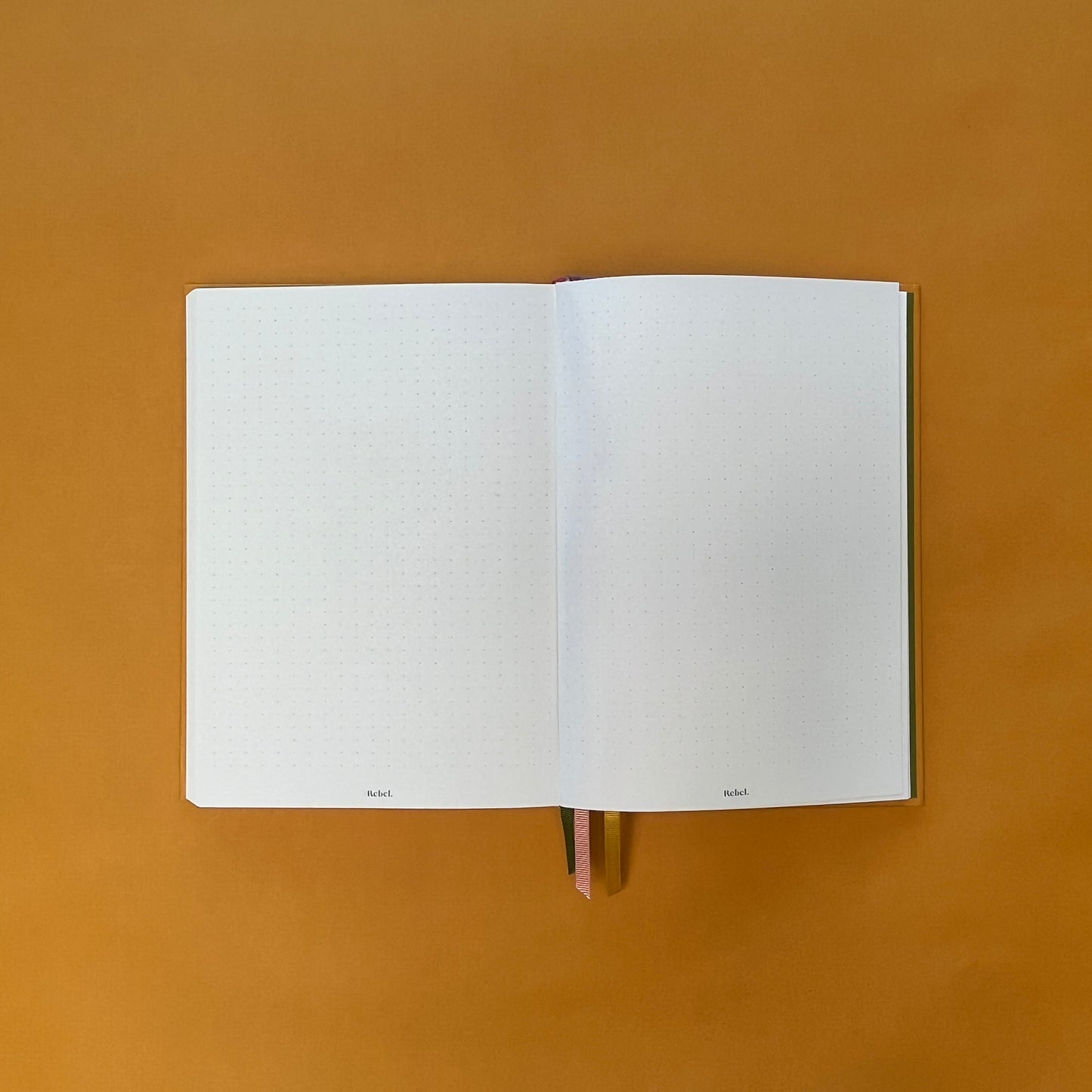 Dotted spread of Rebel Stationery's Gold Seasonal notebook (yellow cover with pink linen spine) on a yellow background