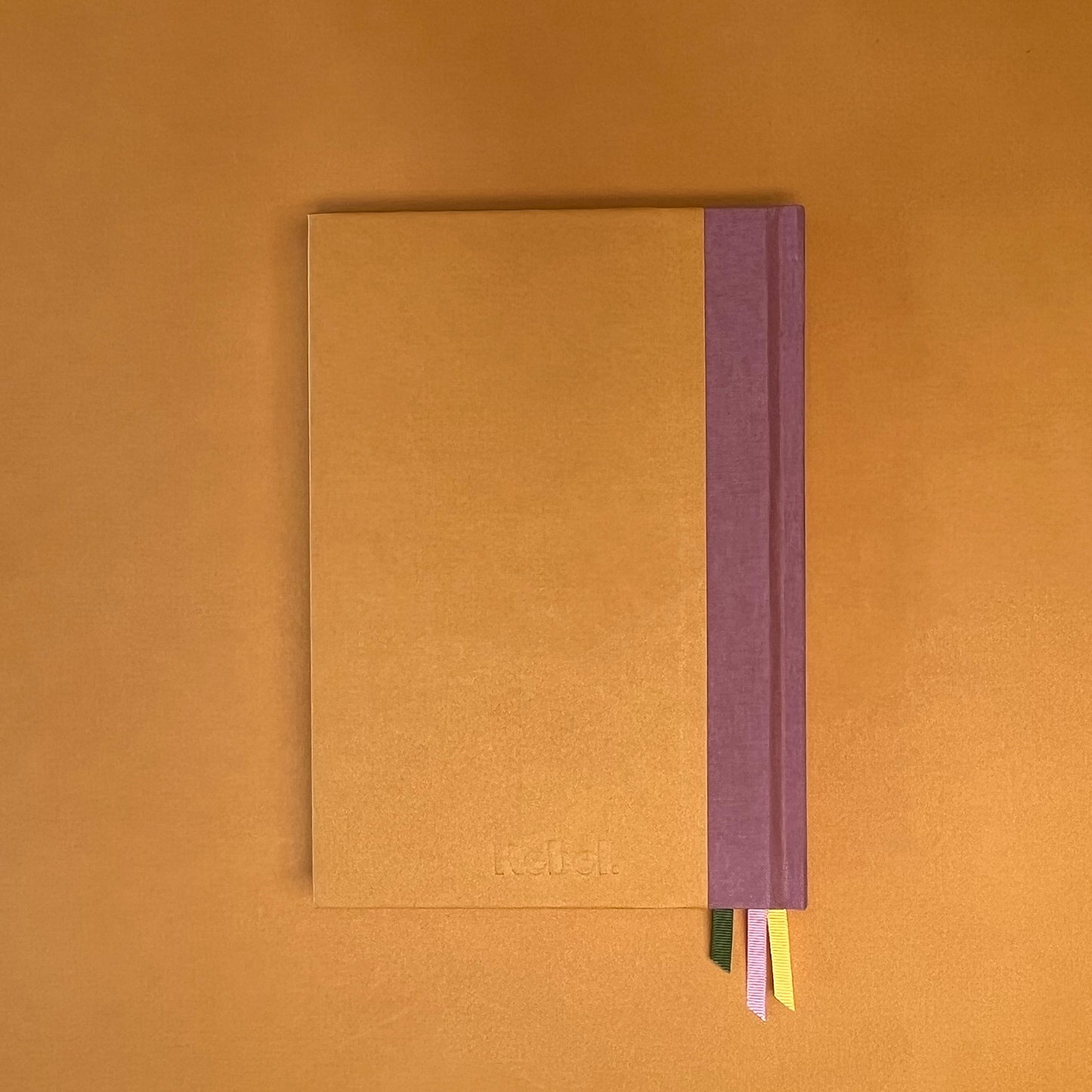 Back cover of Rebel Stationery's Gold Seasonal notebook (yellow cover with pink linen spine) on a yellow background