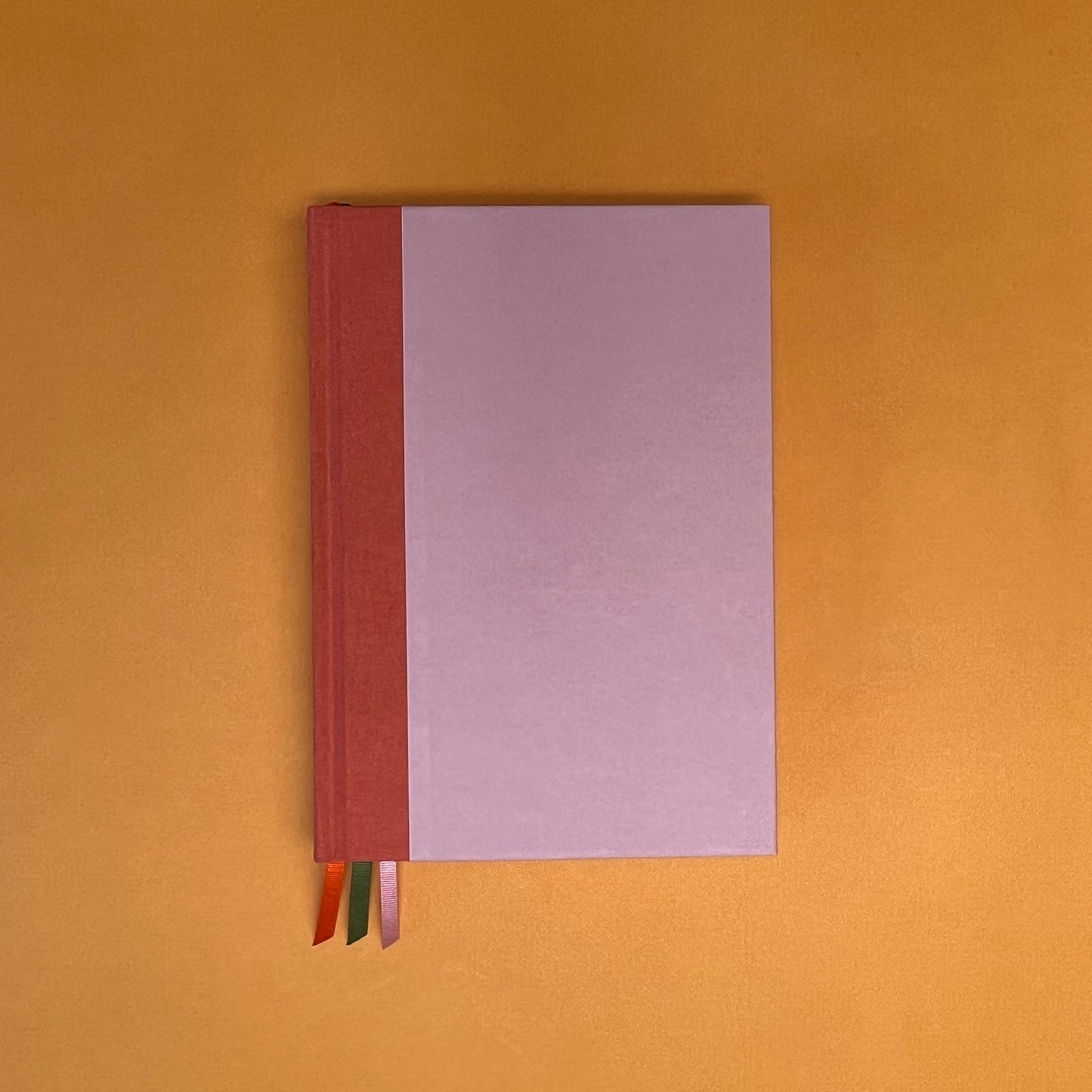 Front cover of Rebel Stationery's Seasonal Rose notebook, a pink A5 with orange-red linen spine, on a yellow background