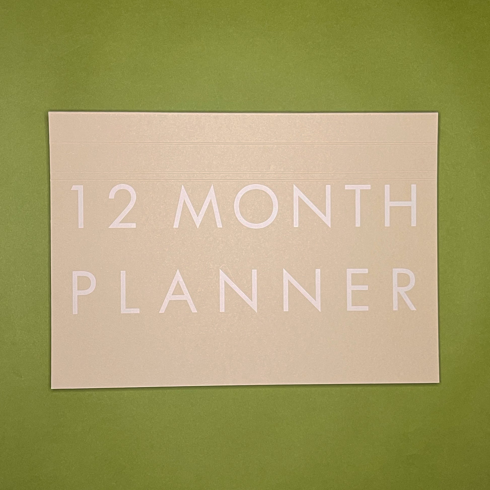 Front cover of Rebel Stationery's Monthly Desk Planner in Stone on a green background