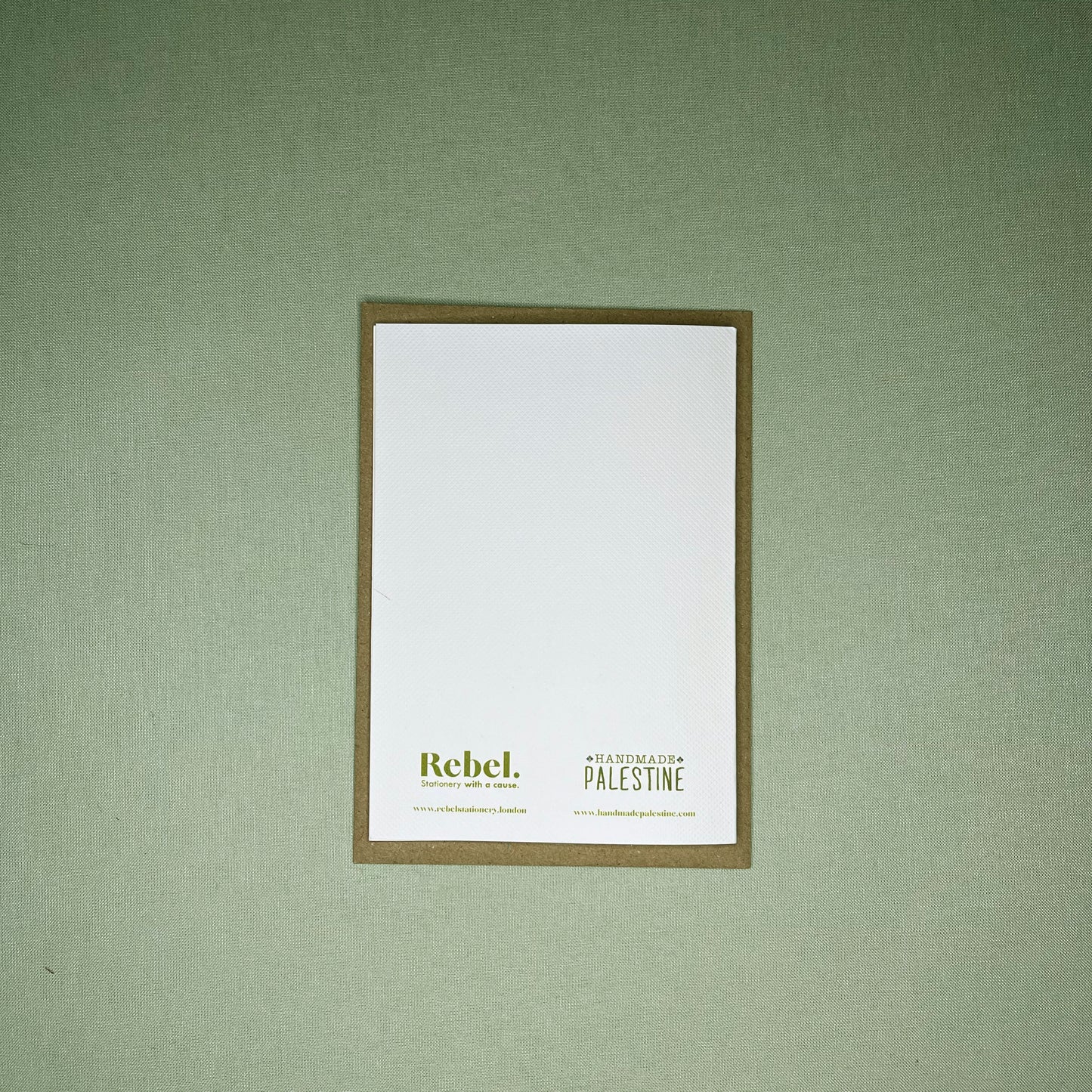 Reverse of A6 greeting card with Rebel Stationery and Handmade Palestine's logos on brown envelope on pistachio linen background