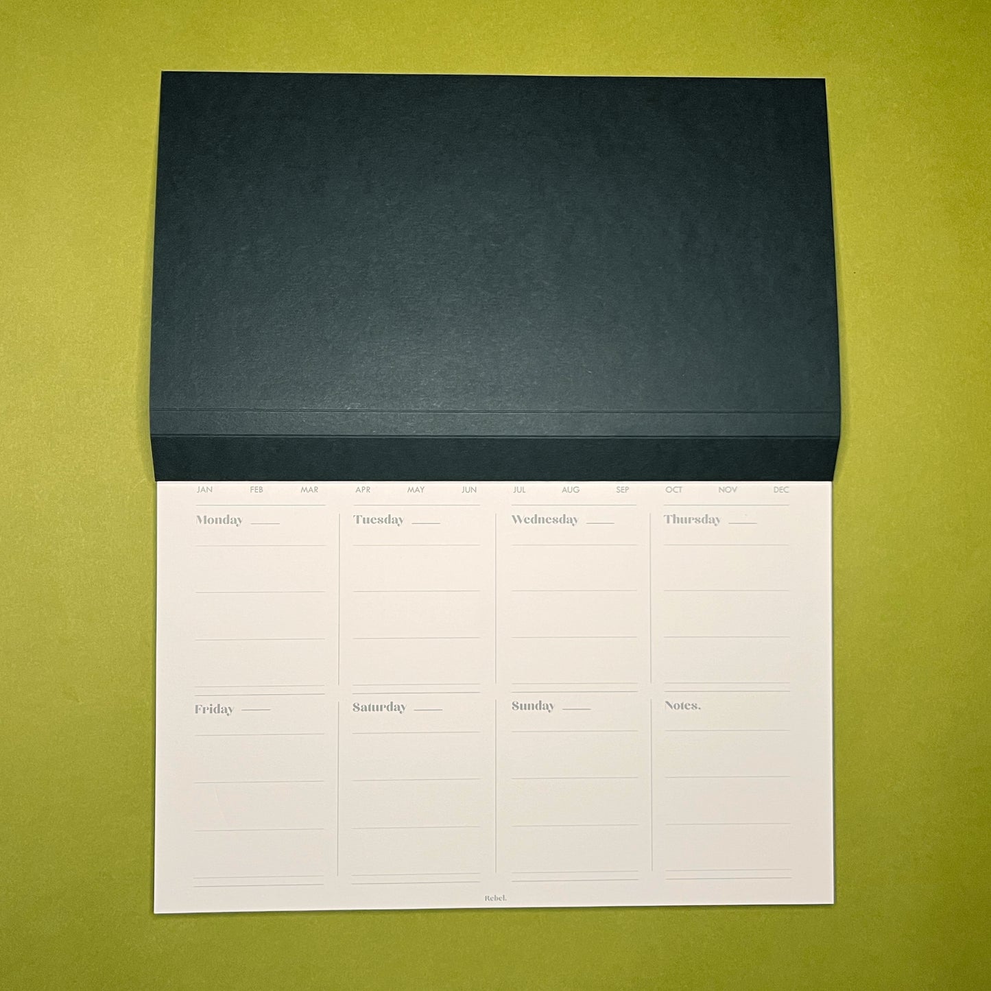 Open shot of Rebel Stationery's A4 Weekly Desk Planner in Ink on green background