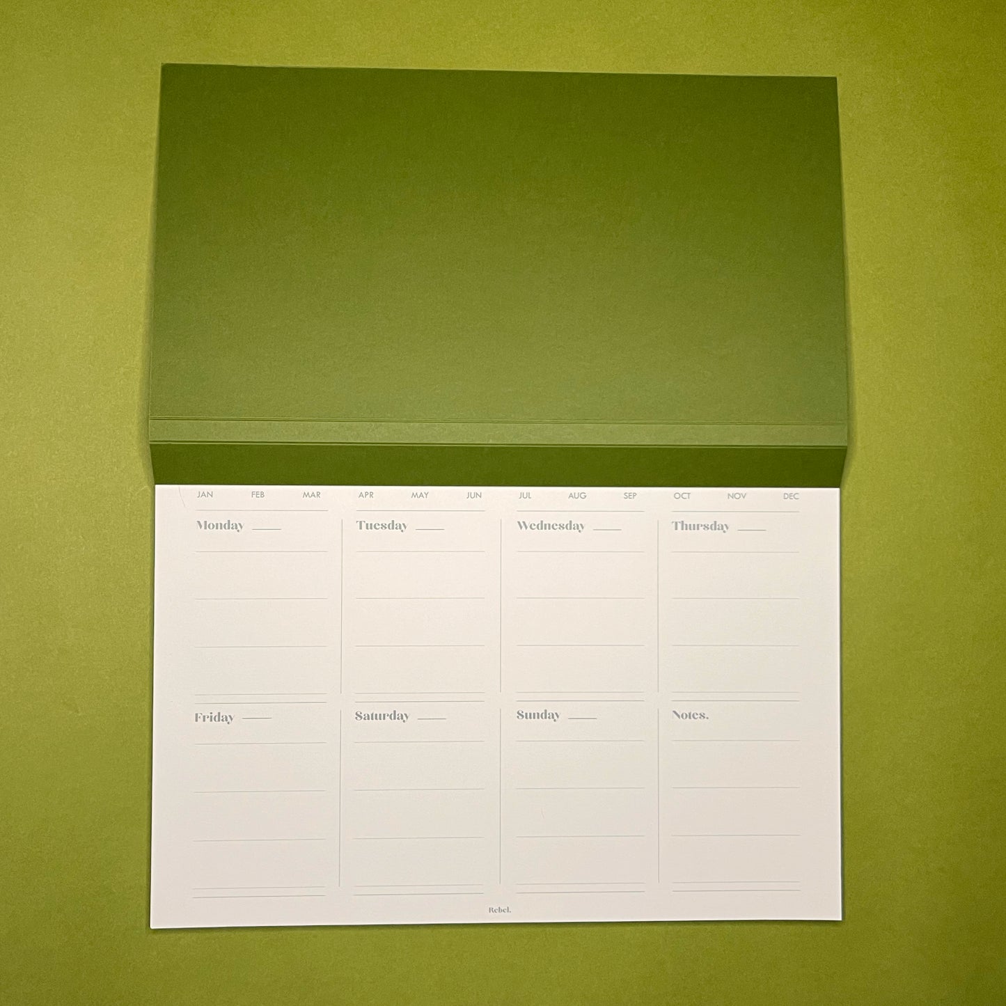 Open shot of Rebel Stationery's A4 Weekly Desk Planner in Ink on green background