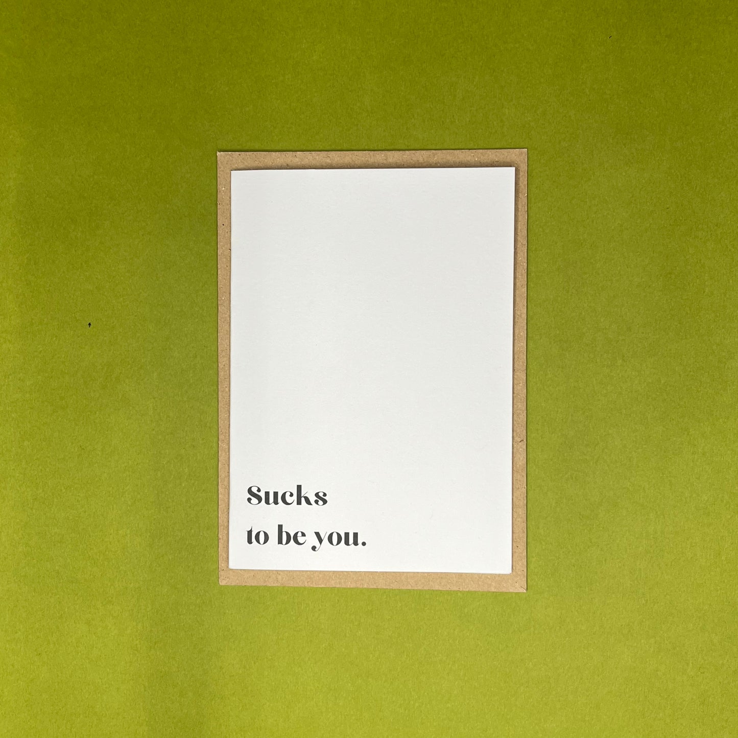 White greeting card with black text on brown envelope on green background