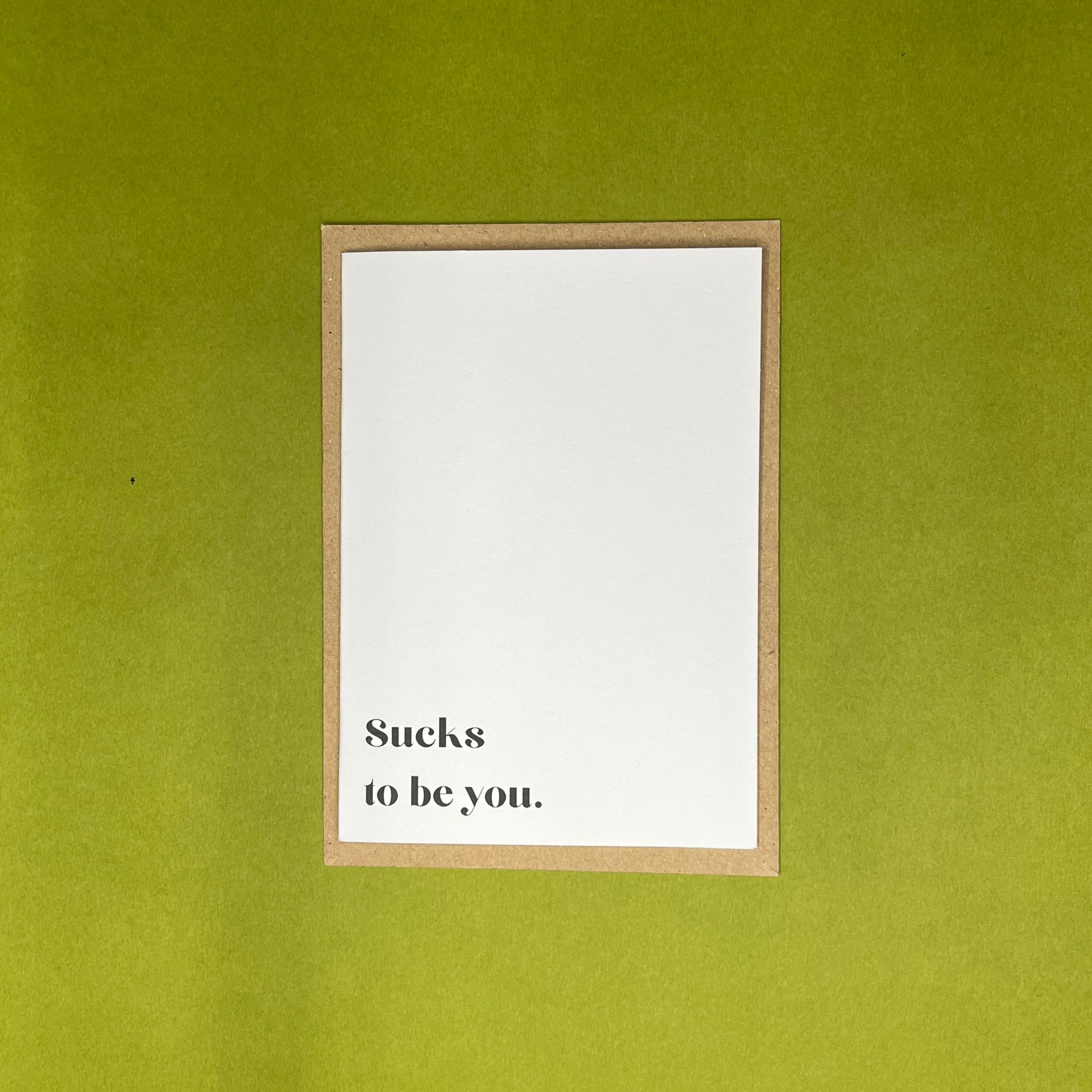 White greeting card with black text on brown envelope on green background