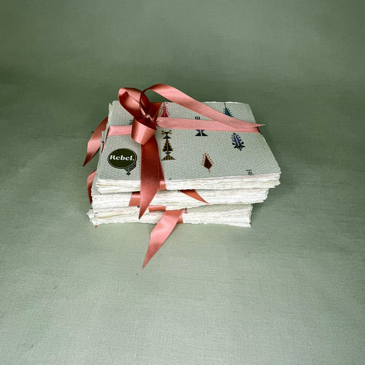 Stack of patterned notelets with a pink ribbon on a green background