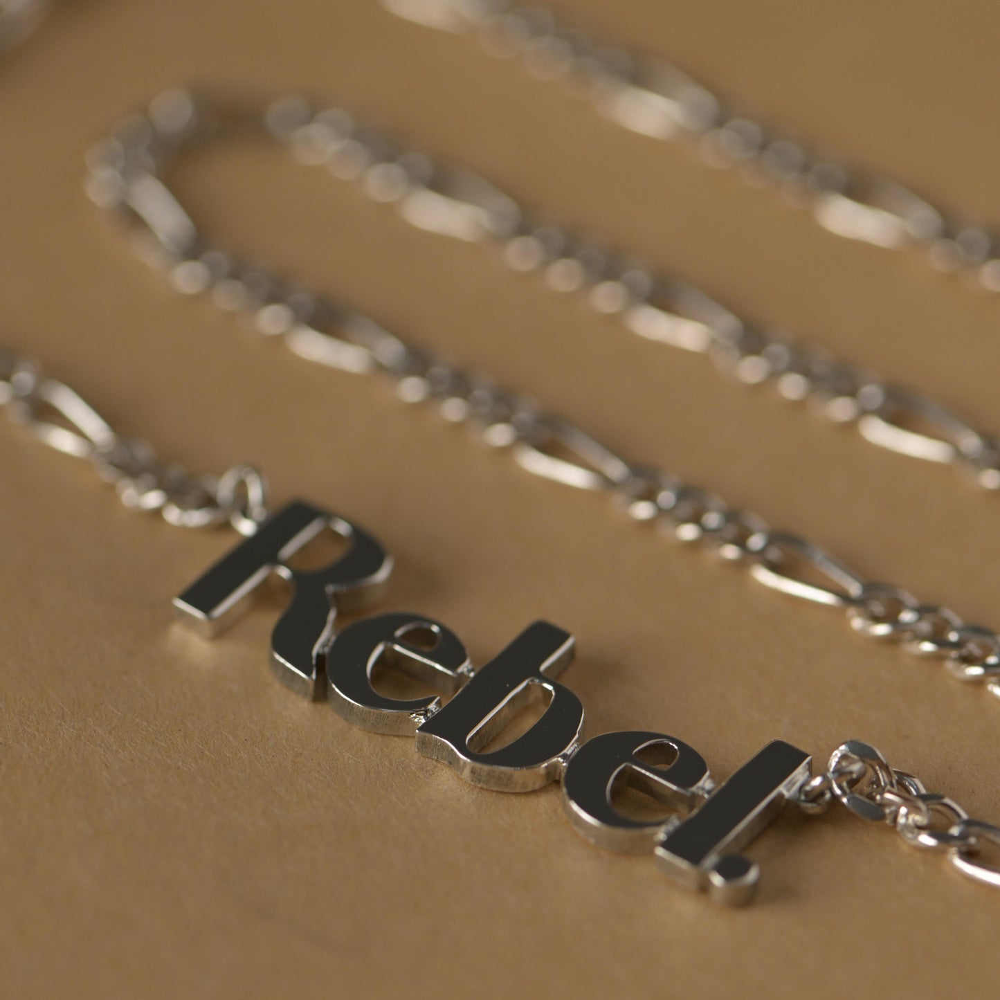 Silver necklace with 'Rebel' pendant on a beige background
