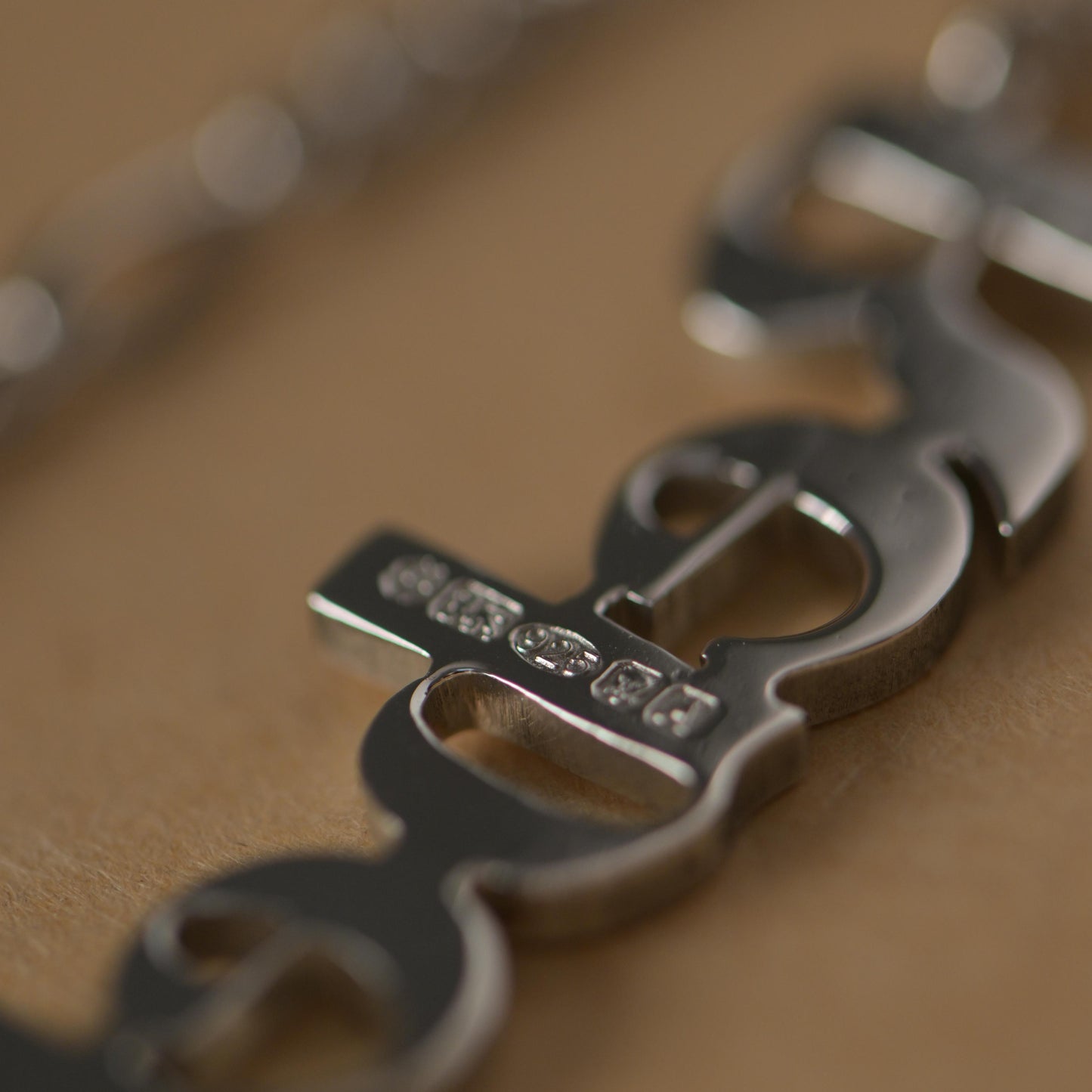 Close-up of the reverse of a silver necklace with hallmarks on a brown surface