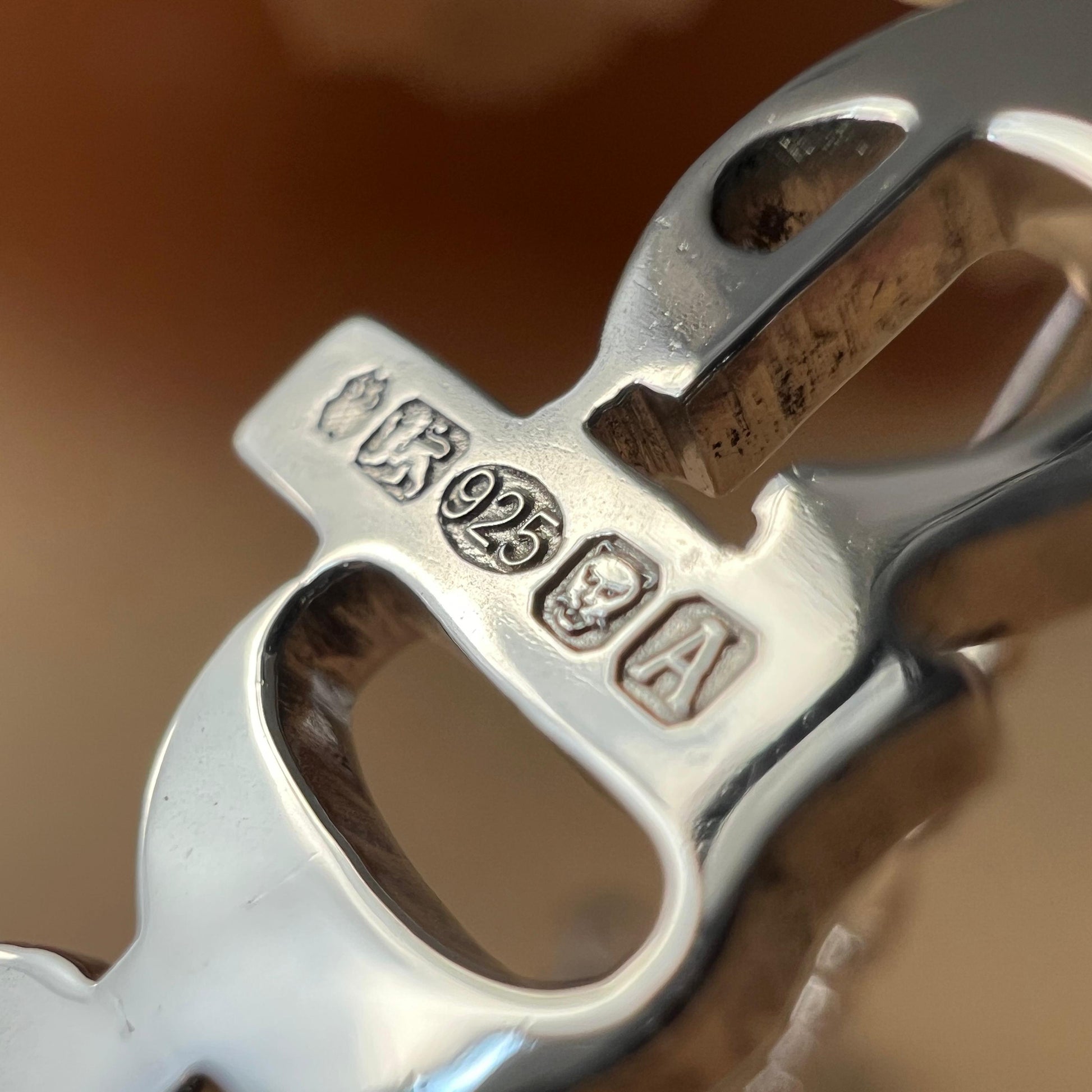 Close-up of the reverse of a silver necklace with hallmarks on a brown surface