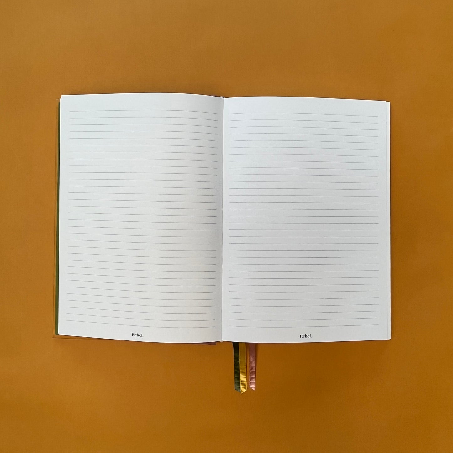 Lined spread of Rebel Stationery's Gold Seasonal notebook (yellow cover with pink linen spine) on a yellow background