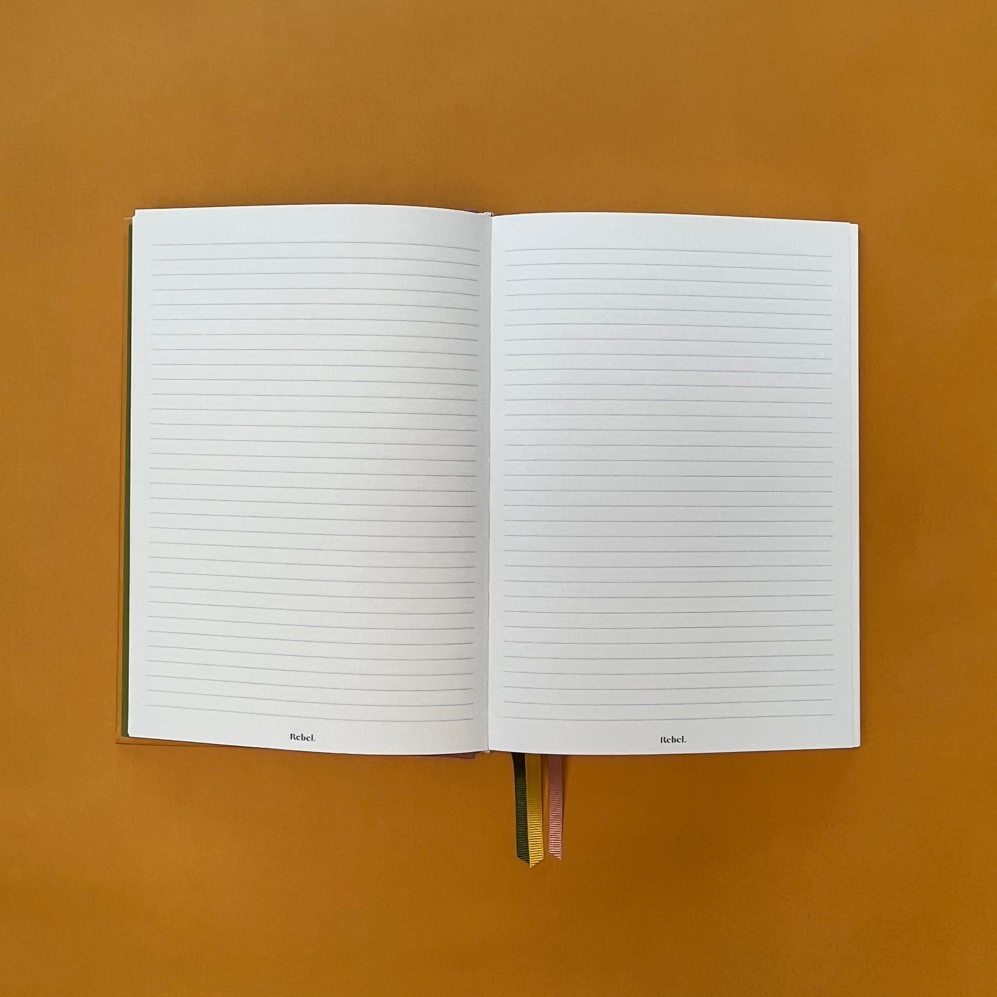 Lined spread of Rebel Stationery's Gold Seasonal notebook (yellow cover with pink linen spine) on a yellow background
