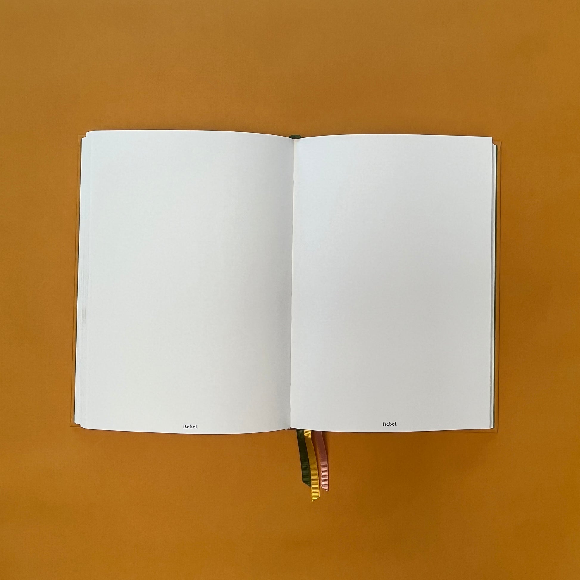 Plain spread of Rebel Stationery's Gold Seasonal notebook (yellow cover with pink linen spine) on a yellow background
