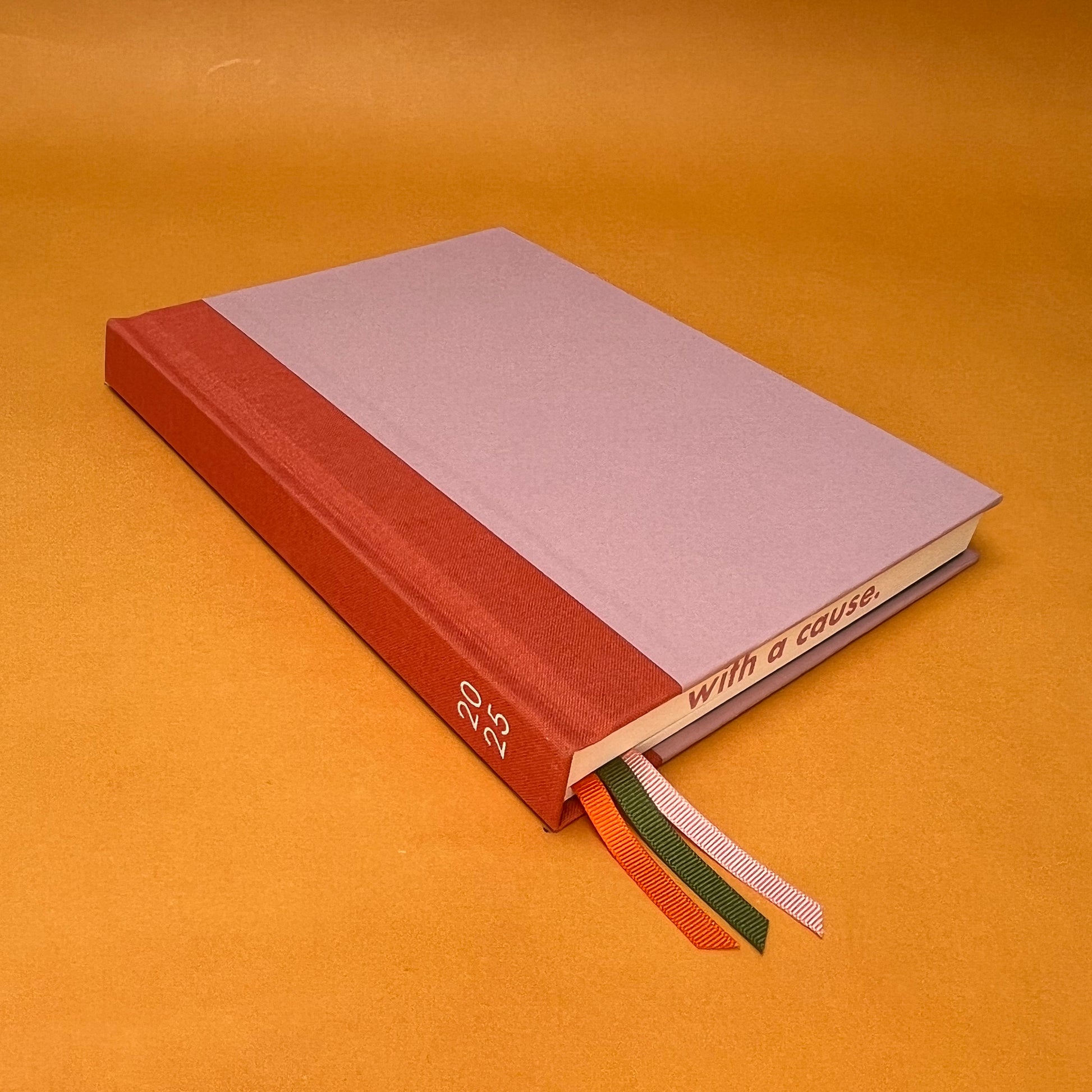 Rebel Stationery's Seasonal Rose notebook, a pink A5 with orange-red linen spine, on a yellow background