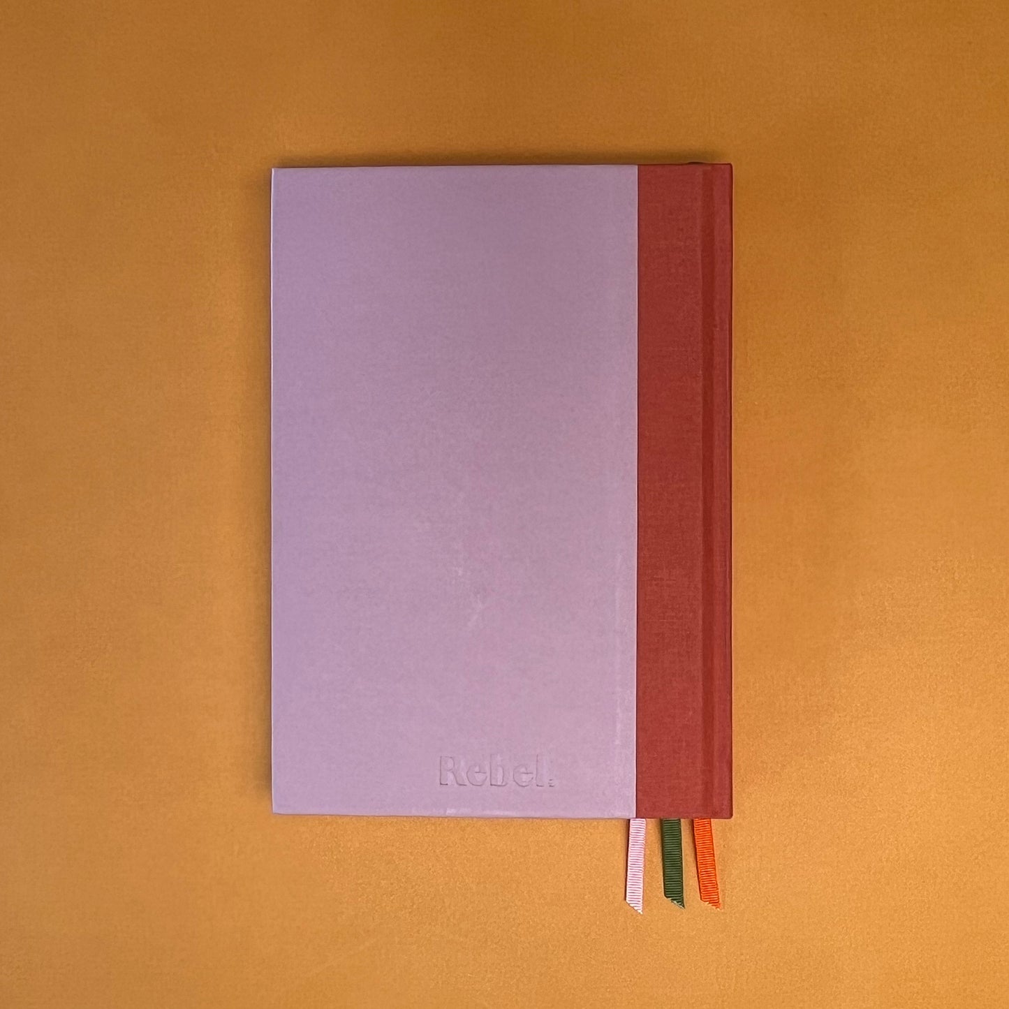 Back cover of Rebel Stationery's Seasonal Rose notebook, a pink A5 with orange-red linen spine, on a yellow background