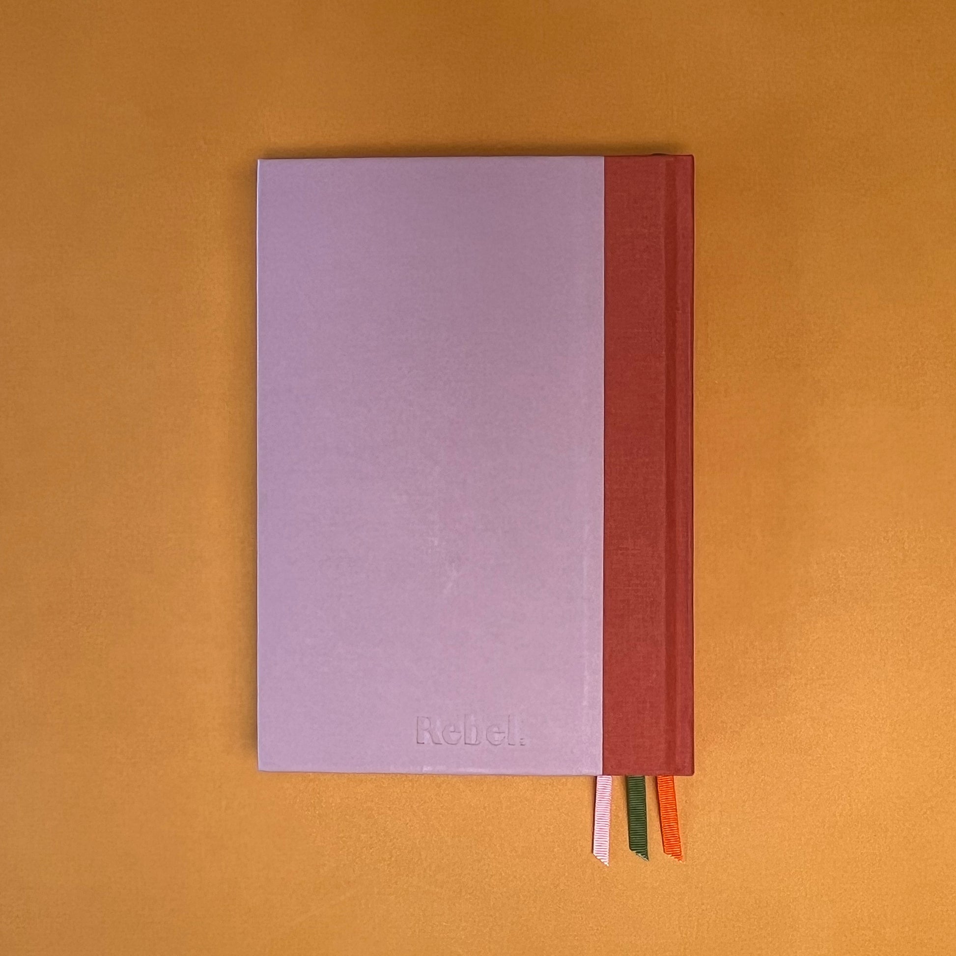 Back cover of Rebel Stationery's Seasonal Rose notebook, a pink A5 with orange-red linen spine, on a yellow background