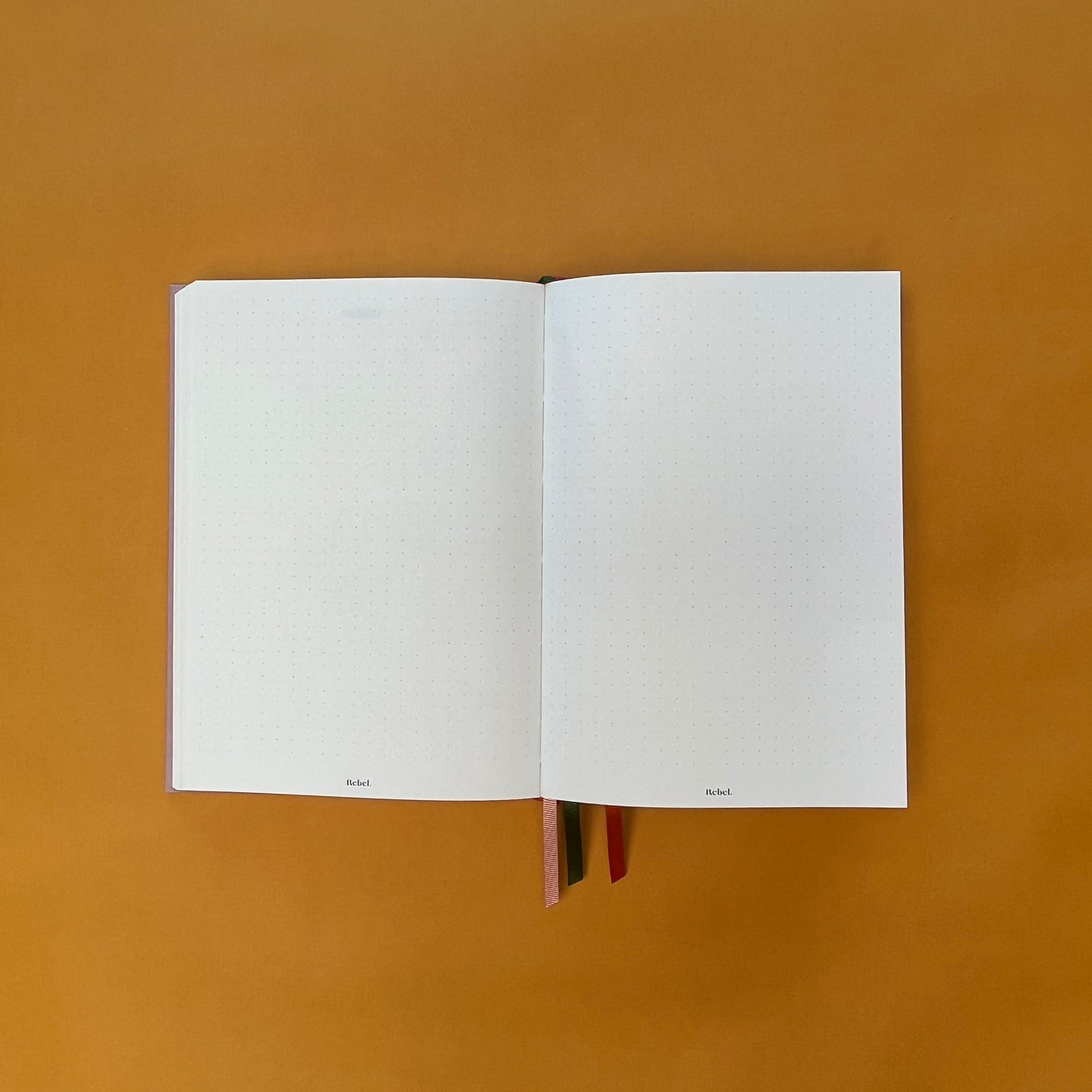Dotted spread of Rebel Stationery's Seasonal Rose notebook, a pink A5 with orange-red linen spine, on a yellow background