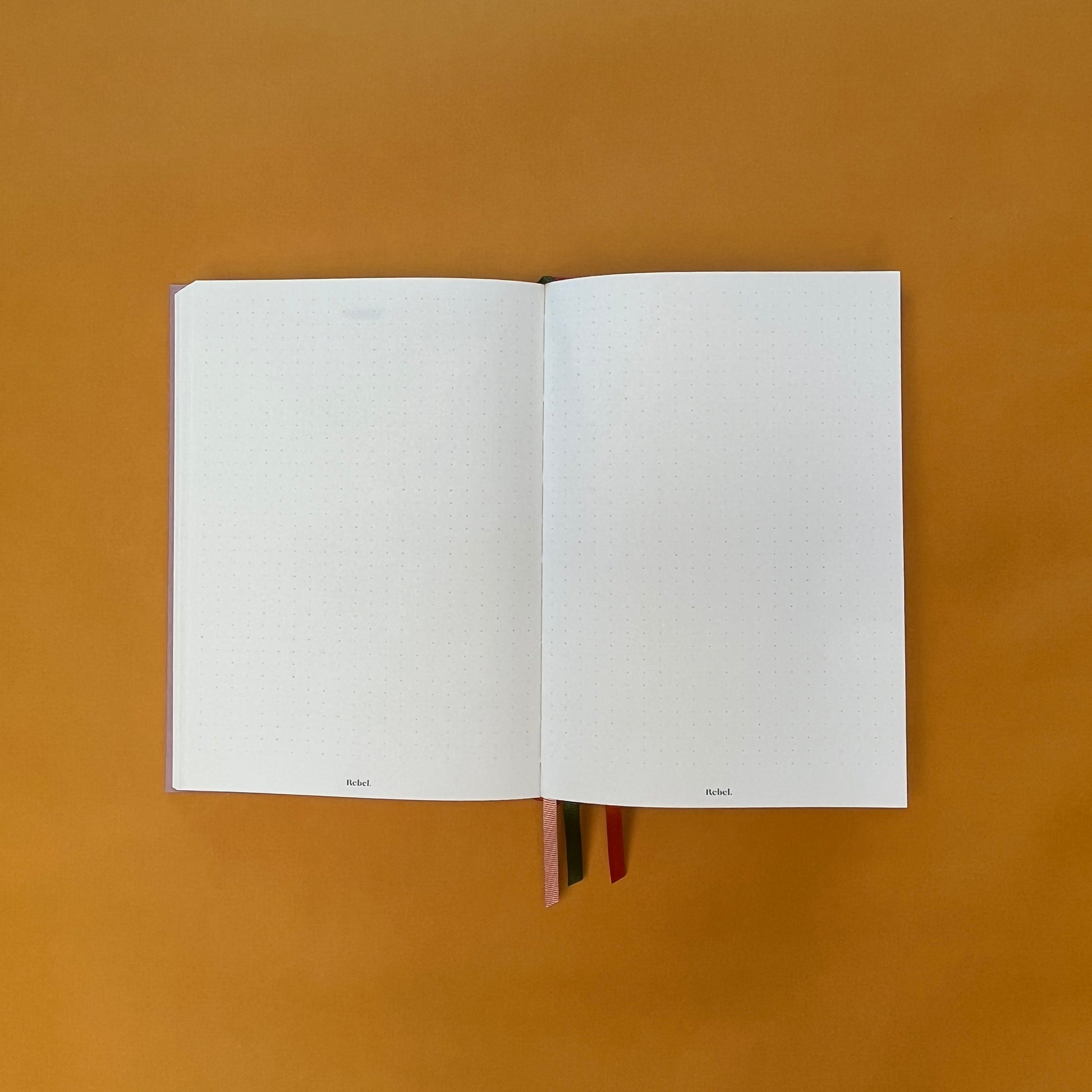 Dotted spread of Rebel Stationery's Seasonal Rose notebook, a pink A5 with orange-red linen spine, on a yellow background