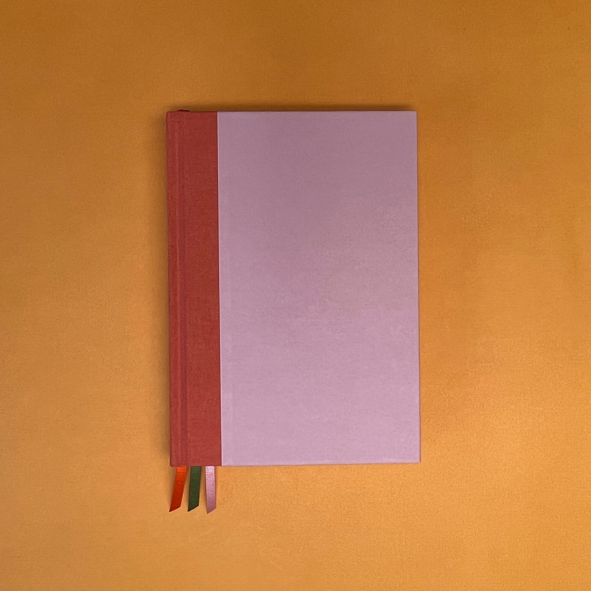 Front cover of Rebel Stationery's Seasonal Rose notebook, a pink A5 with orange-red linen spine, on a yellow background