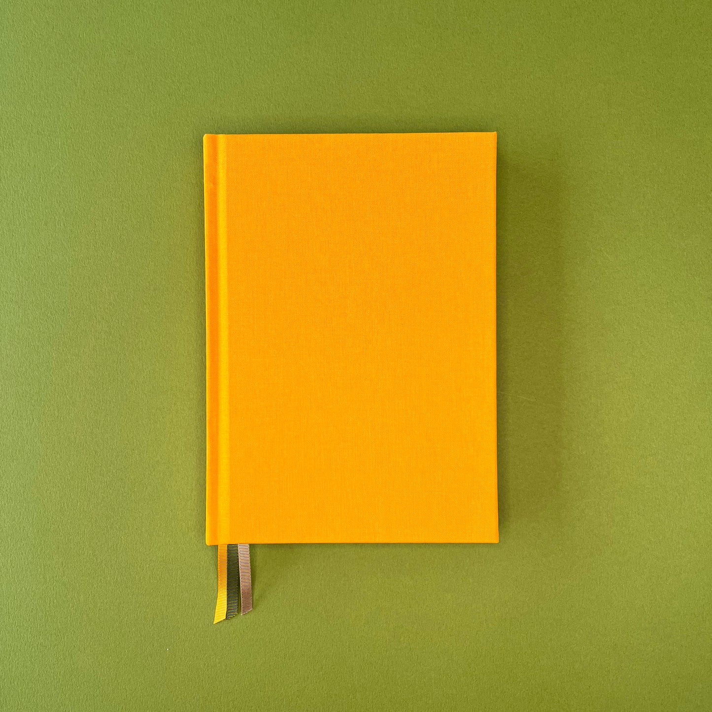 Front cover of Rebel Stationery's Signature A5 notebook in yellow bookcloth, on a green background