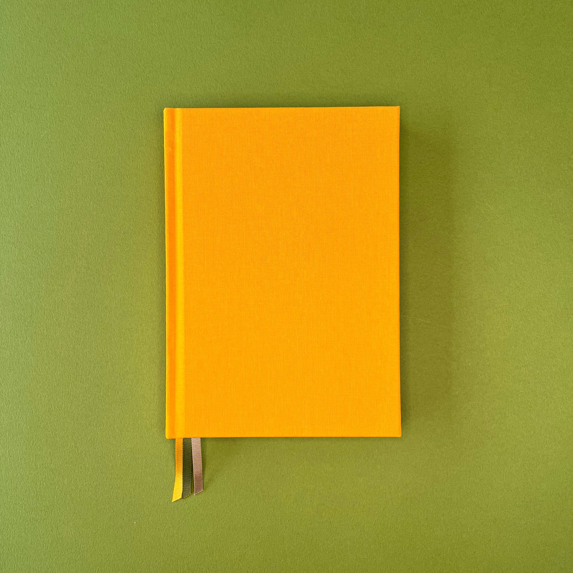 Front cover of Rebel Stationery's Signature A5 notebook in yellow bookcloth, on a green background