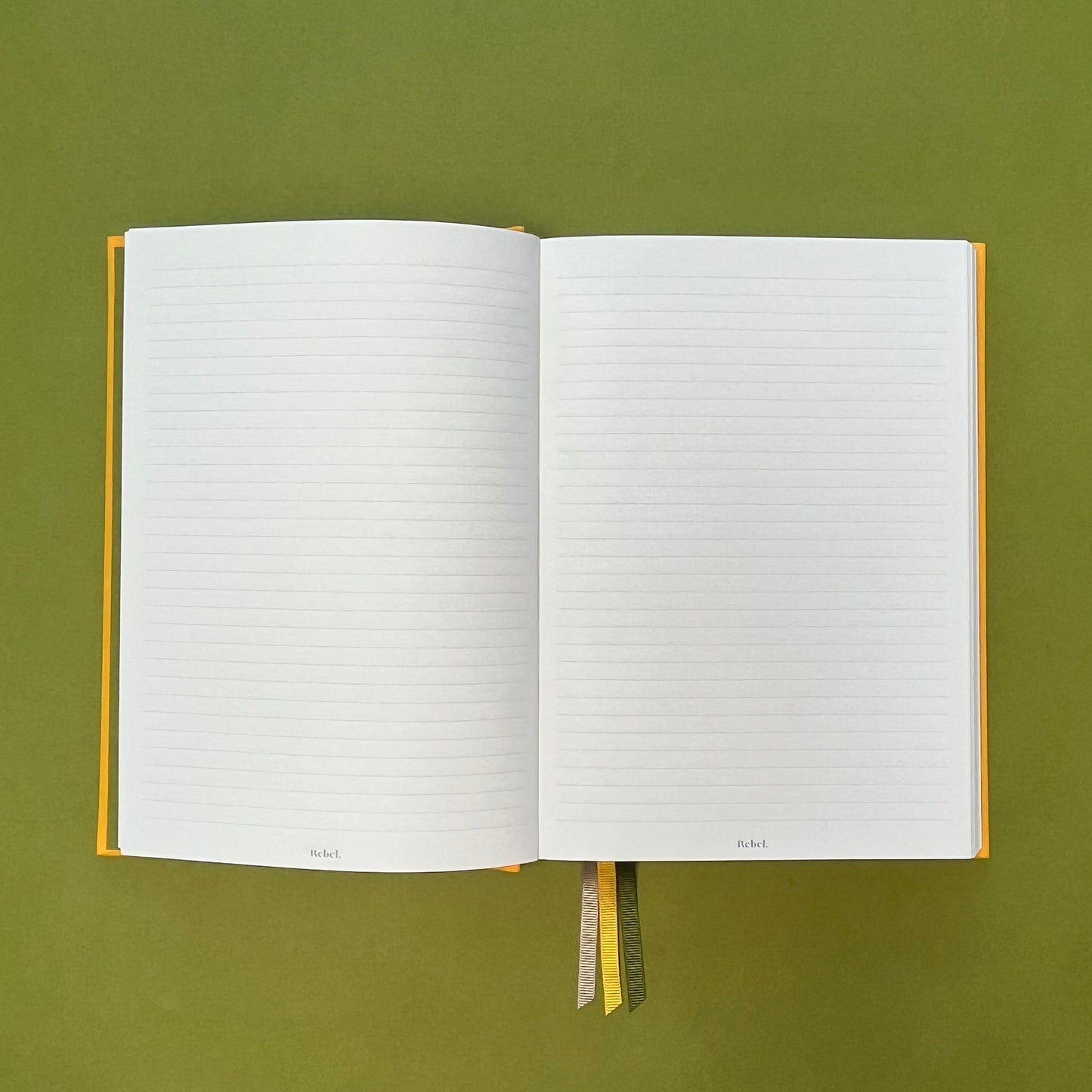 Lined spread of Rebel Stationery's Signature A5 notebook in yellow bookcloth, on a green background
