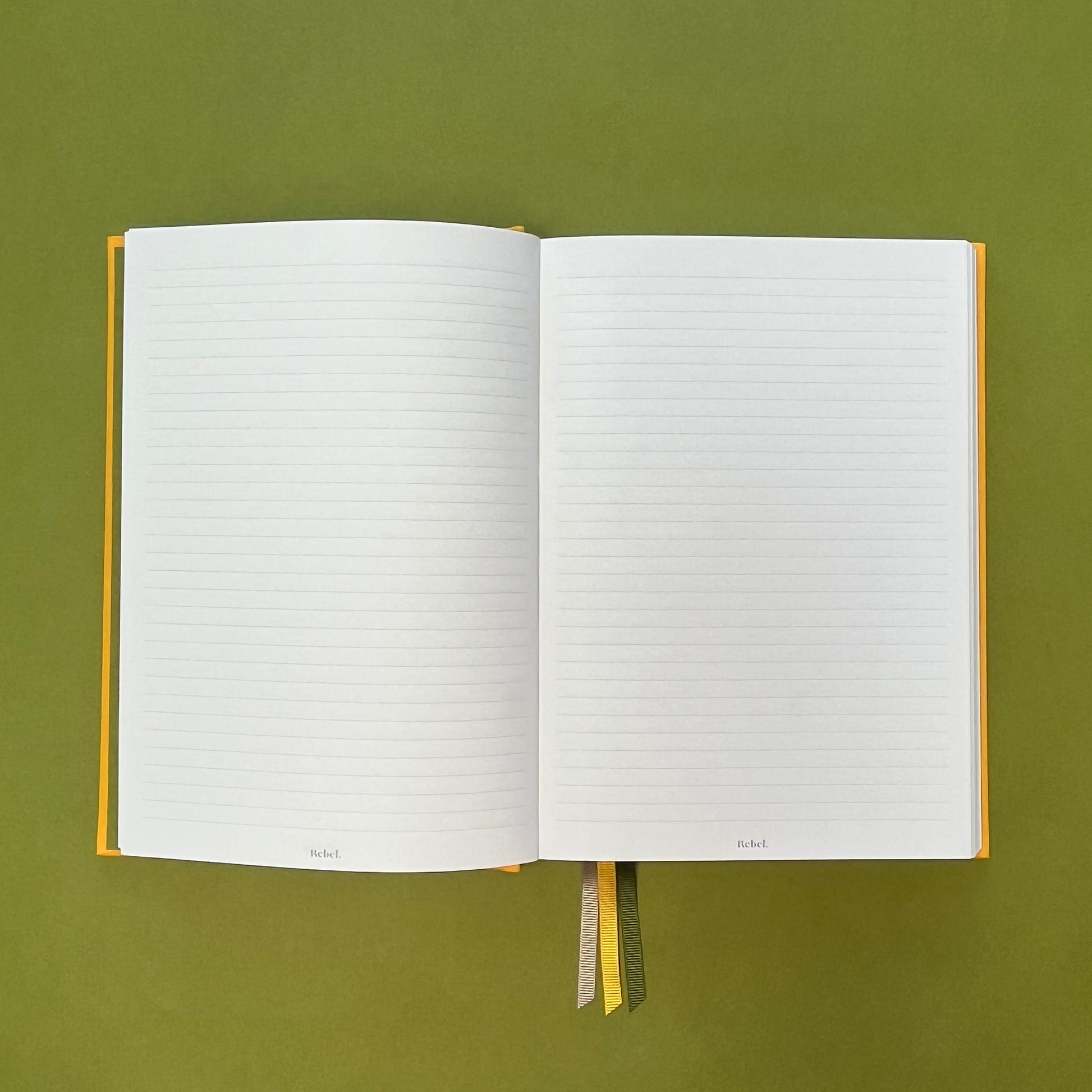Lined spread of Rebel Stationery's Signature A5 notebook in yellow bookcloth, on a green background