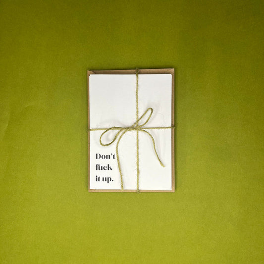 Bundle of white greeting cards with black text tied in green twine on Kraft envelope on green background